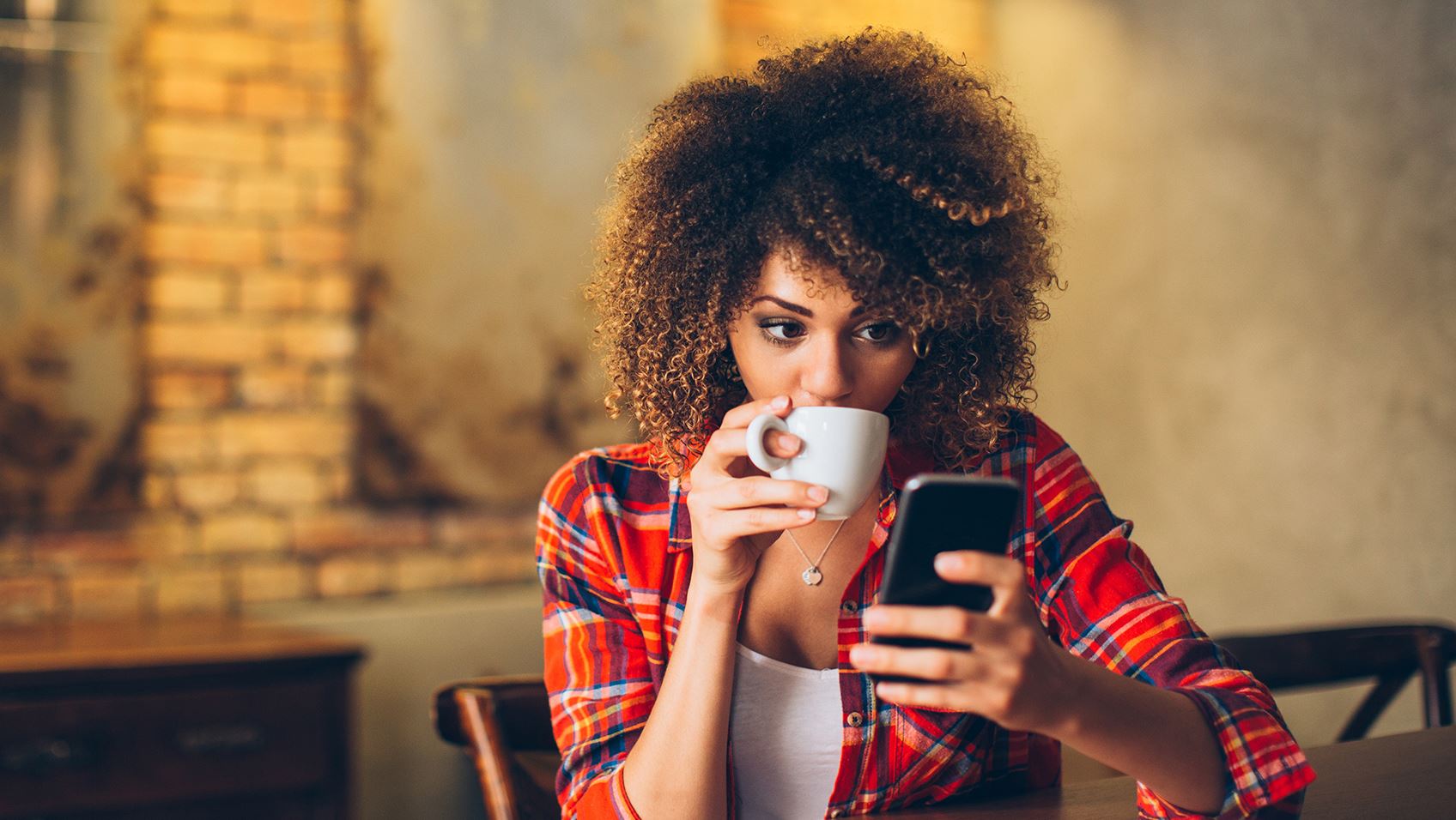 woman drinking coffee and looking at cell phone